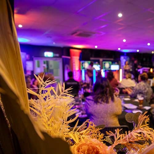 A bunch of flowers in the foreground, in front of an out-of-focus image of an Indigenous business event