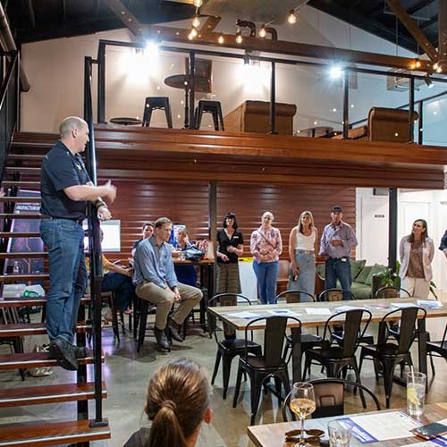 People sit and stand in a room, listening to a man deliver a presentation