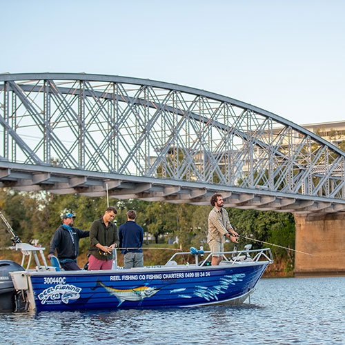 Four people fish from a boat in the Fitzroy River in front of Rockhampton's historic rail bridge